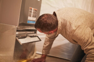 Male home inspector assessing the heating system in the mechanical room of a residential property