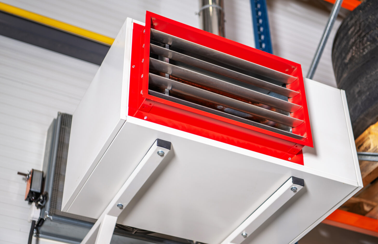 Industrial heater is mounted on a wall in a warehouse setting. The heater has a metal grate and is attached to a metal frame.